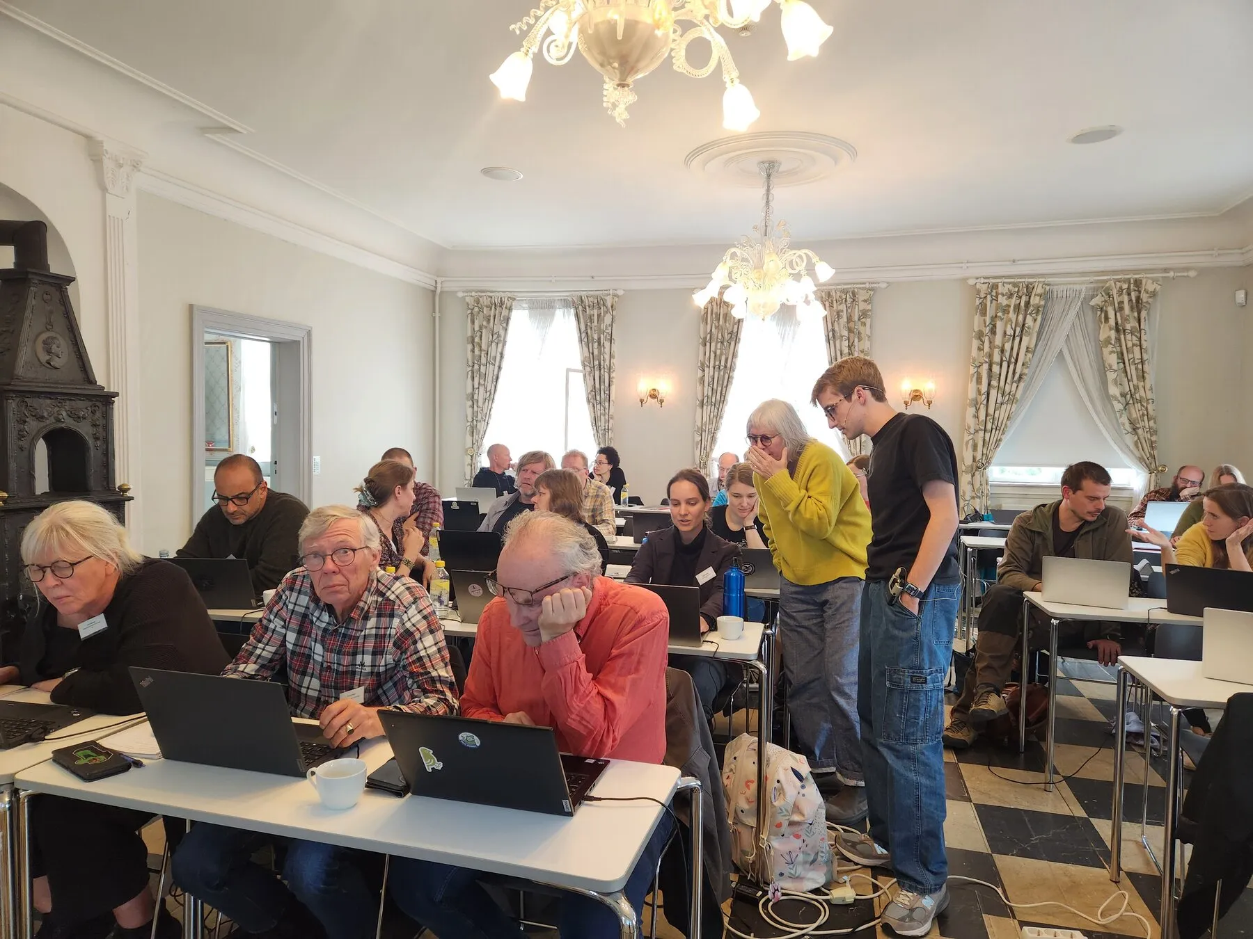 Participants working together at laptops while Grant assists in the workshop room