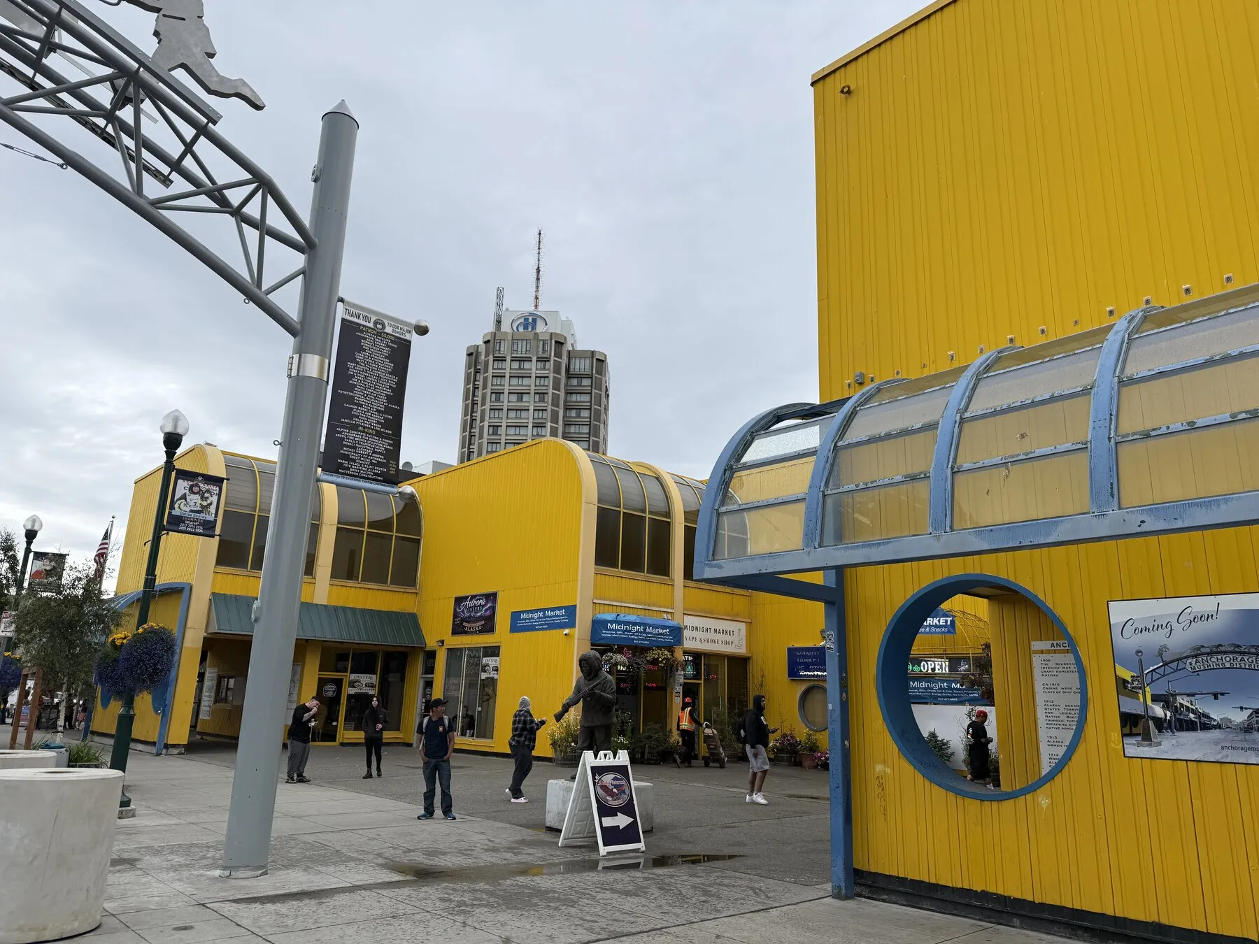 A bright yellow building and storefronts in downtown Anchorage beneath a cloudy sky