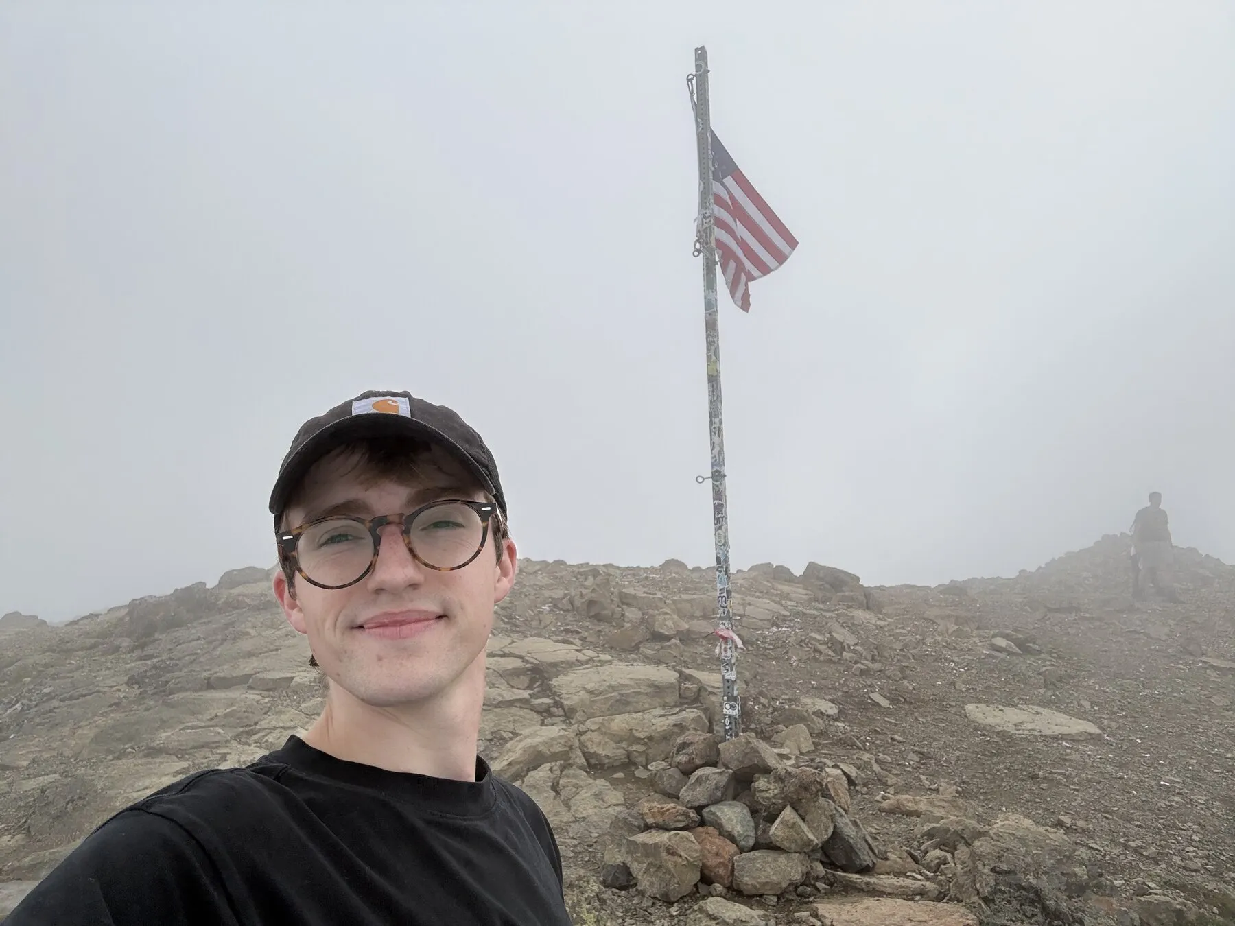 Grant at the rocky top of Flattop with a flag disappearing into the mist