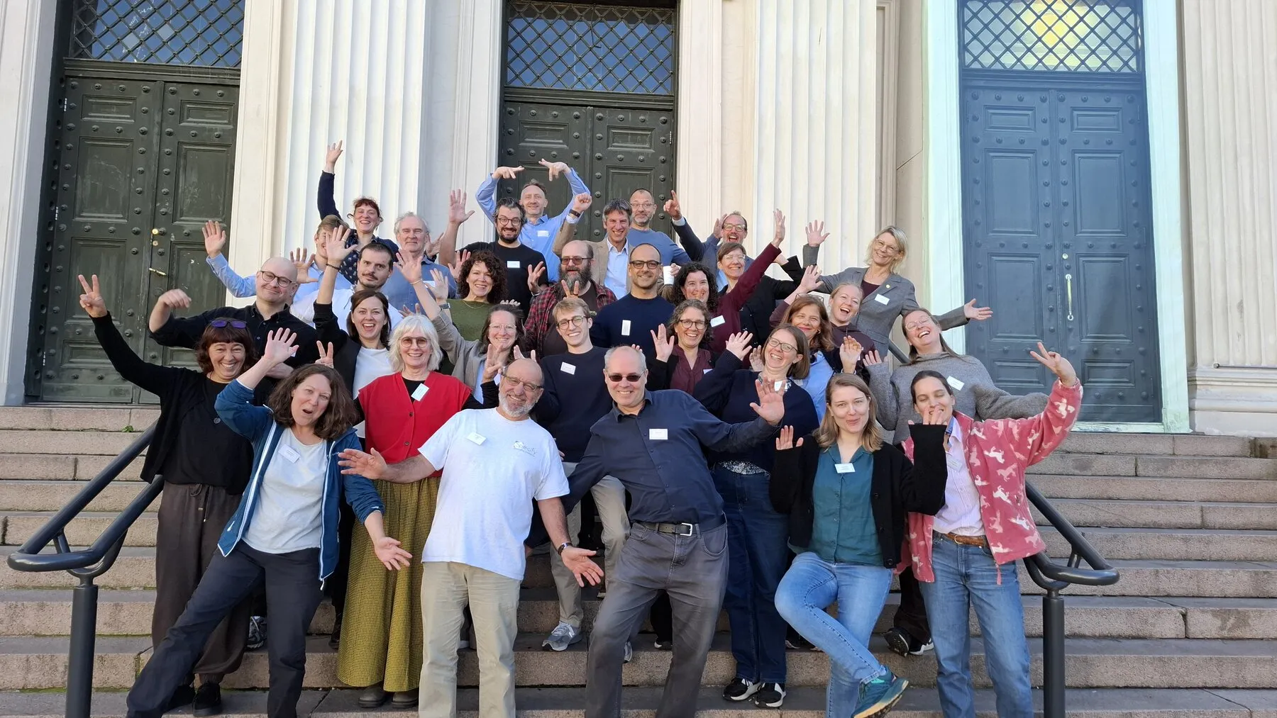 Summit participants smiling, waving, and posing on the steps outside
