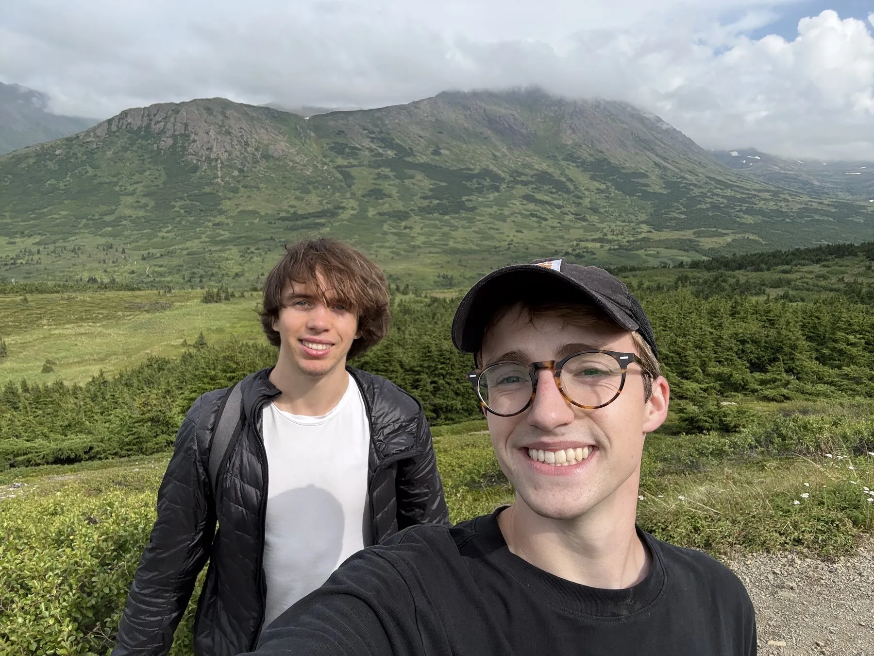 Us on the hiking trail with green mountain slopes behind them