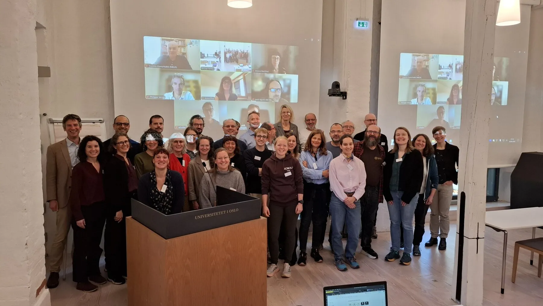 Summit participants in the meeting room, with online participants visible on the screen
