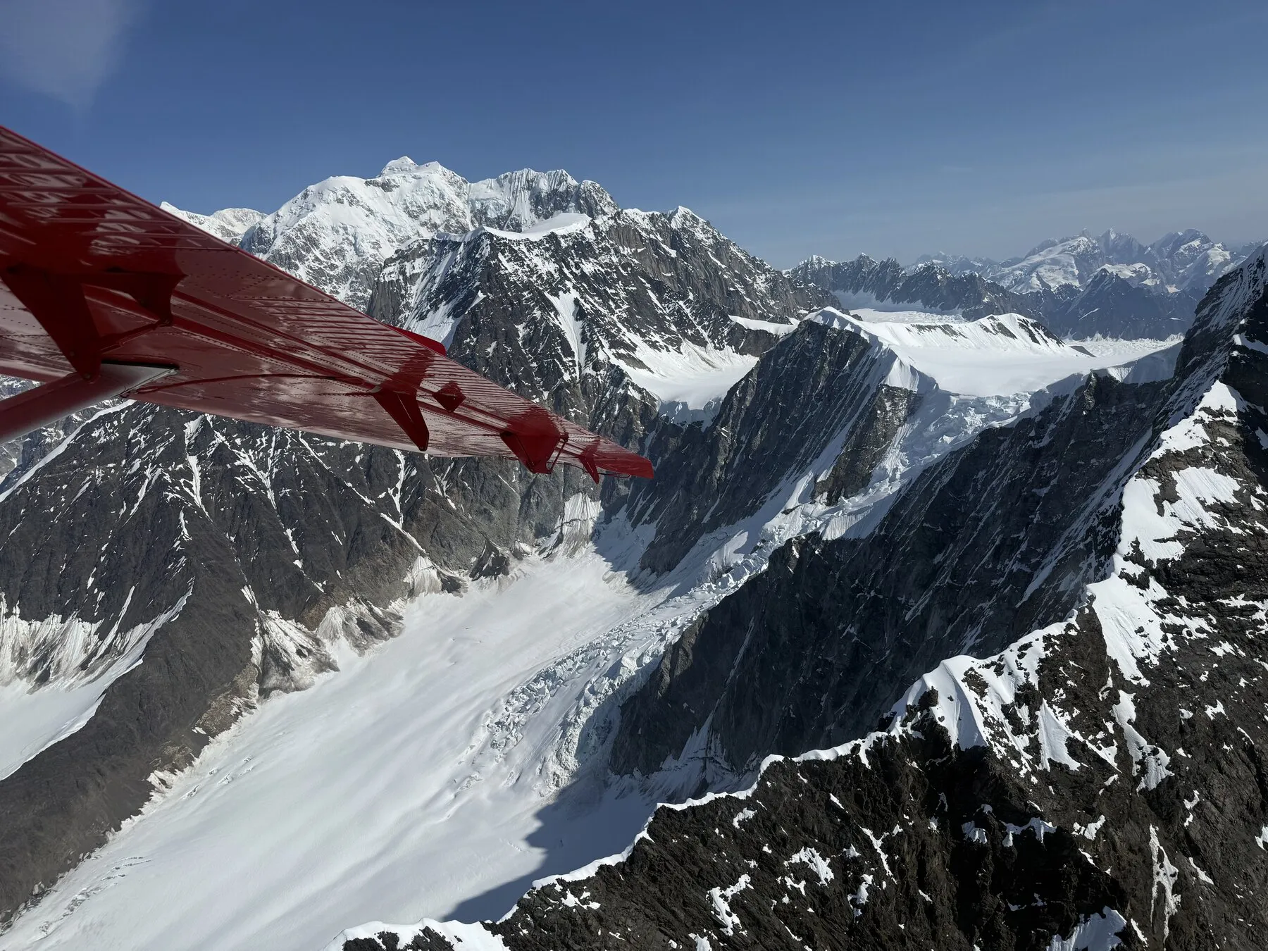 Snow-covered mountains and steep ridges viewed beneath the red wing of the plane